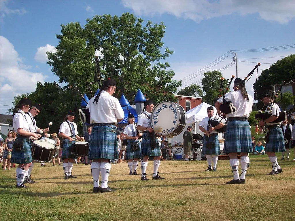 Maine St. Andrew's pipers and drummers in Maine State Tartan kilts playing together in a circle at an outdoor summer festival